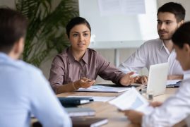 Attractive,Indian,Ethnic,Businesswoman,With,Businessman,Partner,Talking,In,Boardroom Group of people sitting at the table and discussing staffing agency insurance programs.